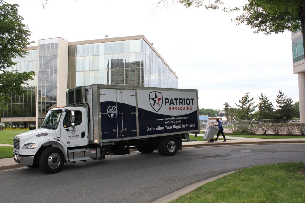Patriot Shredding Off-Site Shredding in a company truck, outside a large office building.
